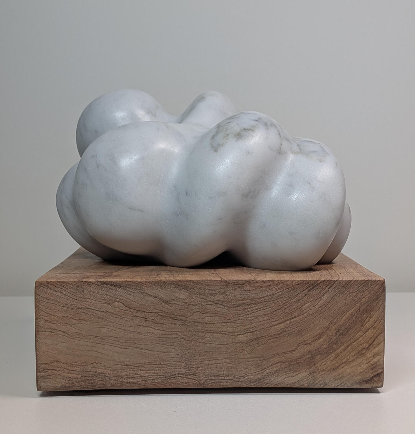 Hemelreiking (t 'Oofd Omogestrekt) Abstracte vorm verzonken in sokkel. Tweestrijd tussen aarde en hemel. Satijnmat Ordinario marmer , Venetiaans olijfhout 20×20 cm (h: 19 cm) | Status: Beschikbaar